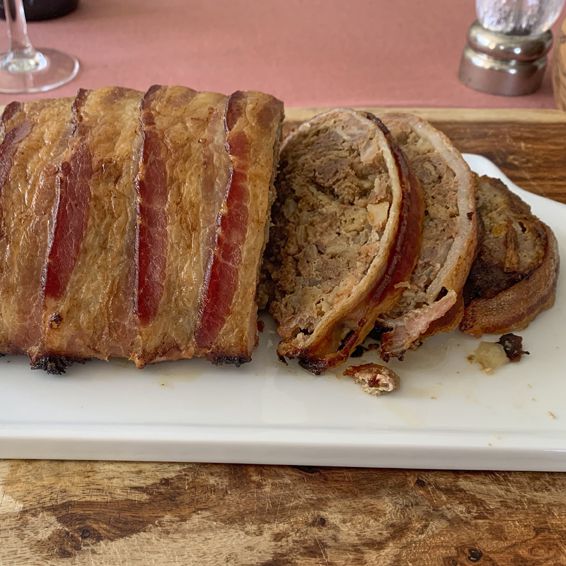 Loaf of bacon wrapped meatloaf with a few slices resting on a cutting board.
