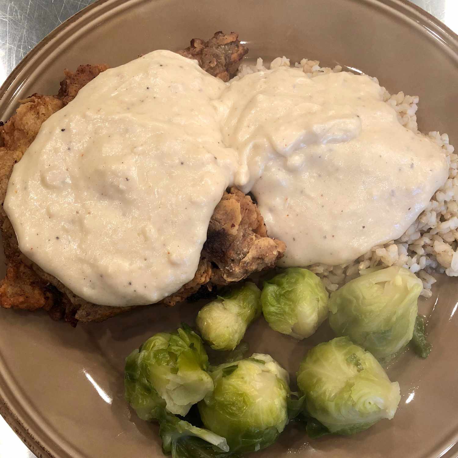 white gravy over breaded meat with rice and Brussels sprouts