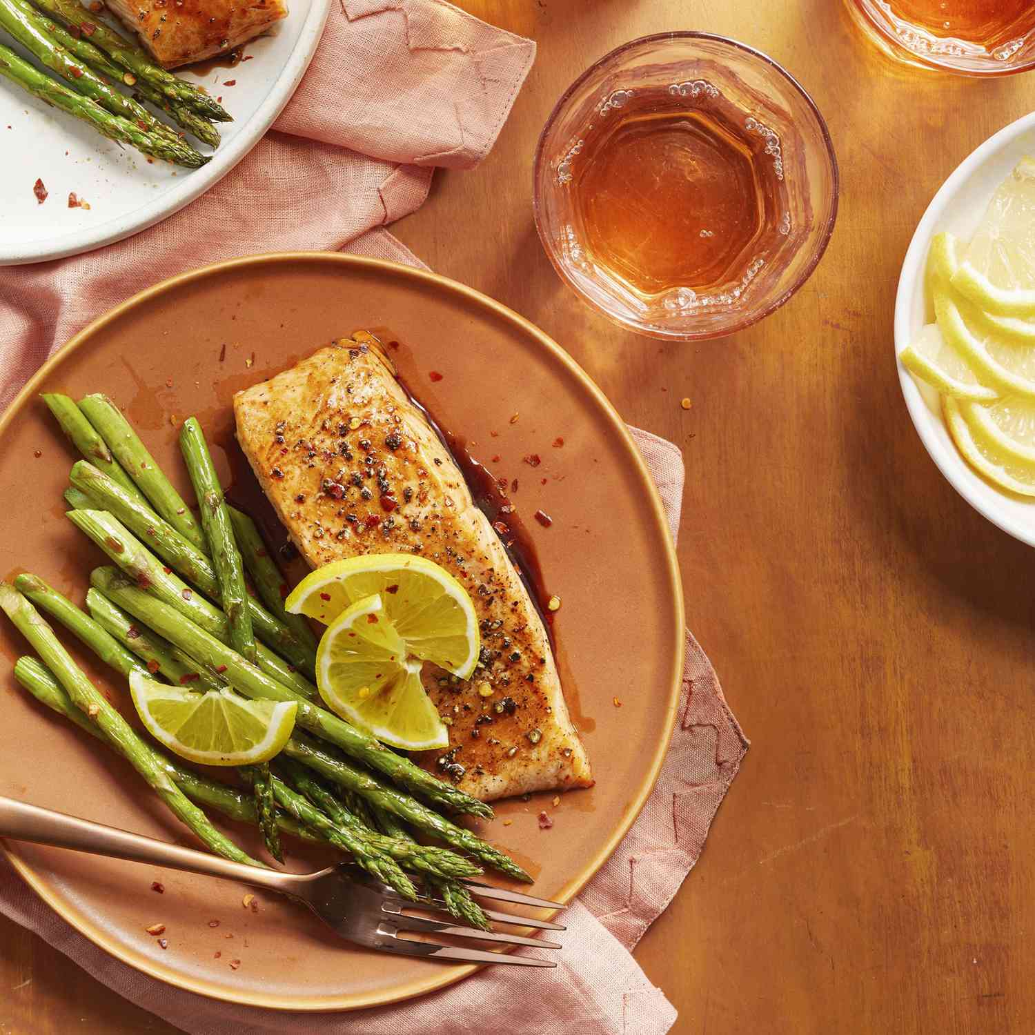 Soy and Honey-Glazed Salmon filet served with a side of roasted asparagus topped with think lemon wedges and red pepper flakes