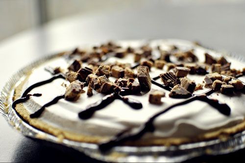 side view of a pie topped with whipped topping, chopped peanut butter cups, and stripes of chocolate sauce