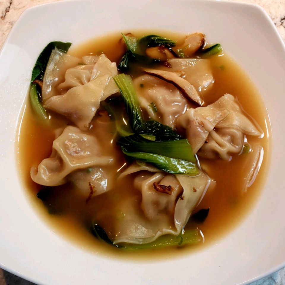 top-down view of a bowl of wonton soup with sliced shiitake mushrooms and baby bok choy