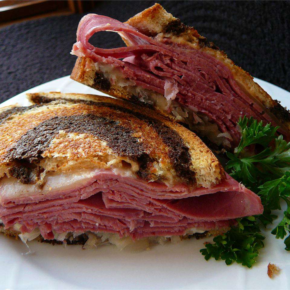 side view of a grilled and sliced reuben sandwich layered with pastrami, sauerkraut, and swiss cheese