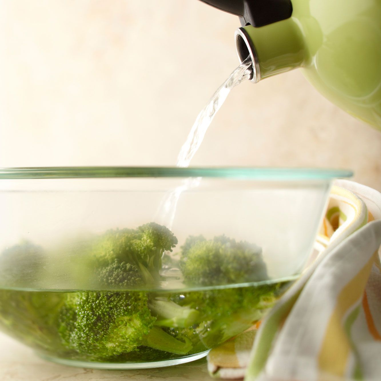 broccoli in glass bowl with boiling water being poured over it