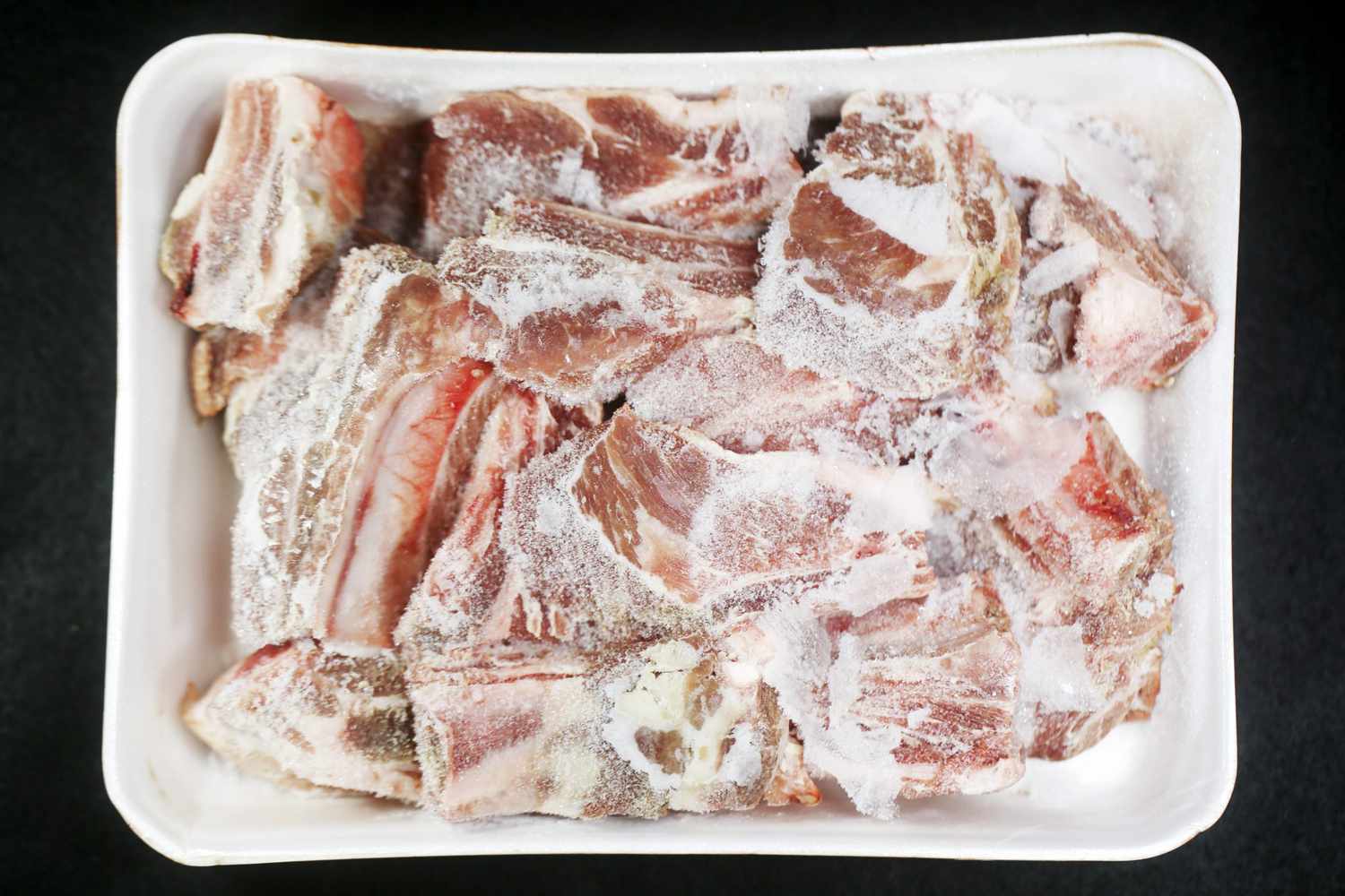Frozen spareribs in disposable plastic tray on black background