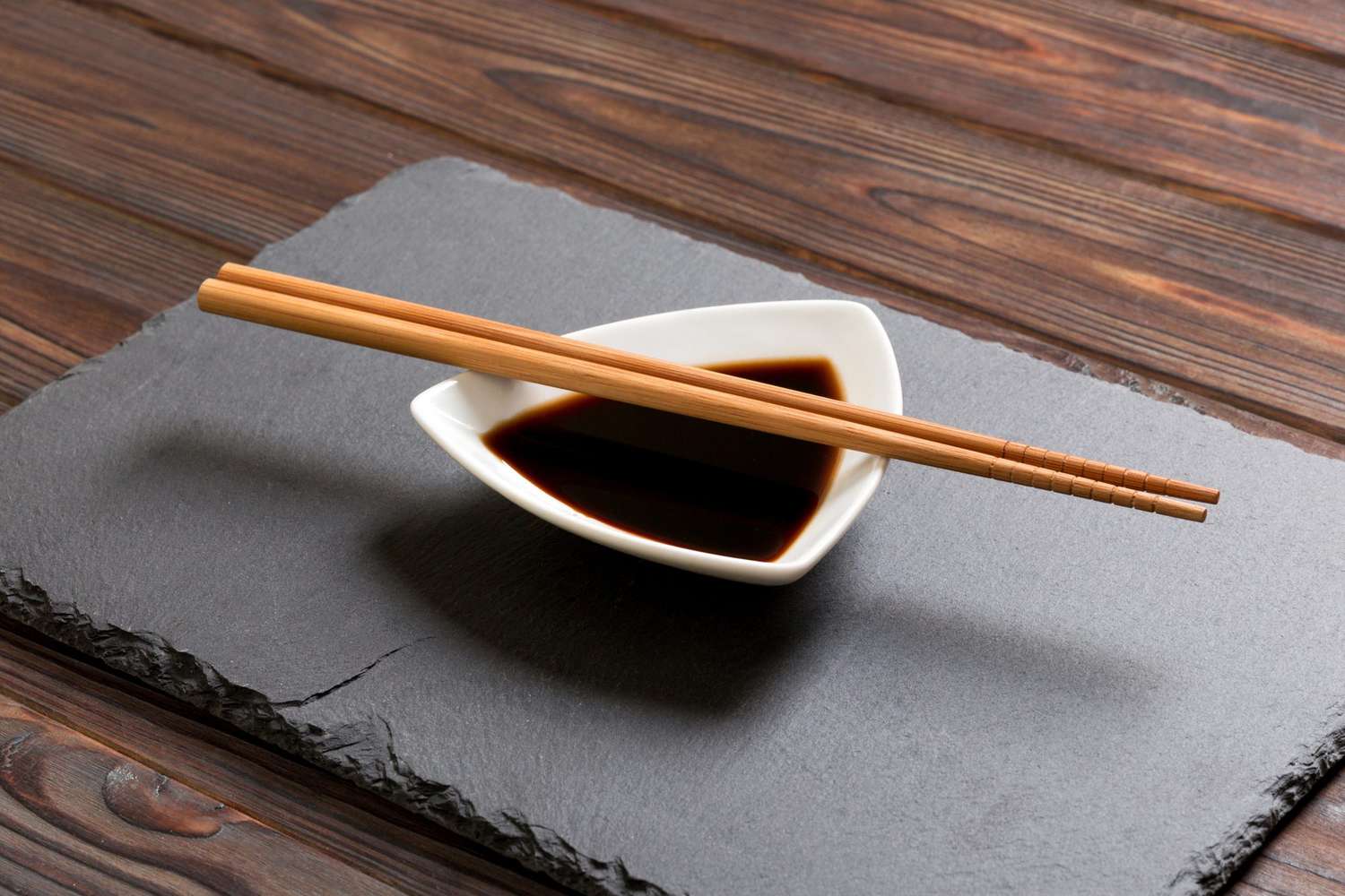Chopsticks and tamari in a white dish on a wooden background