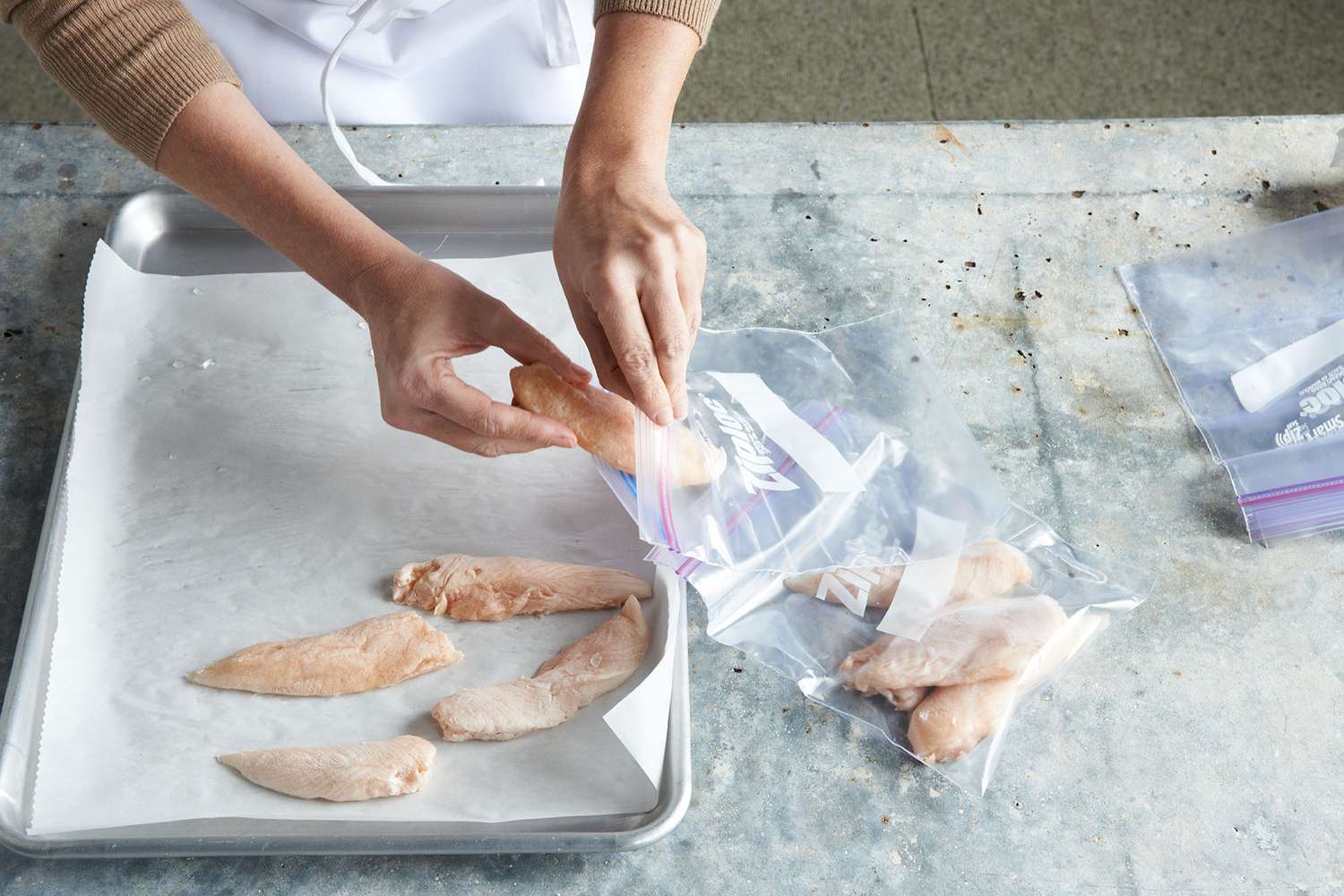 person putting frozen chicken tenderloins on baking sheet with parchment paper