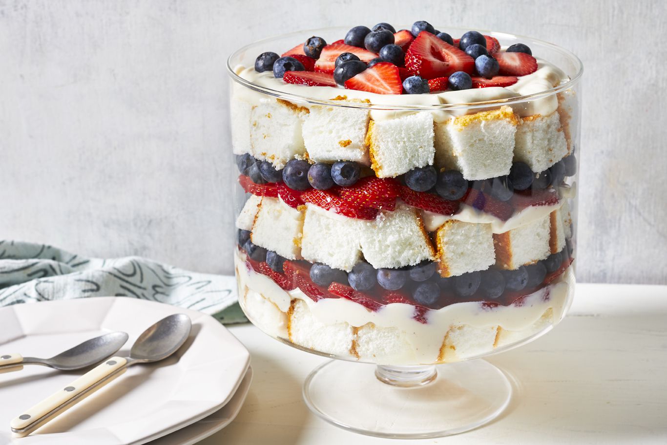 a gorgeous trifle layered with cake, fresh blueberries and fresh strawberries. stack of plates nearby for serving