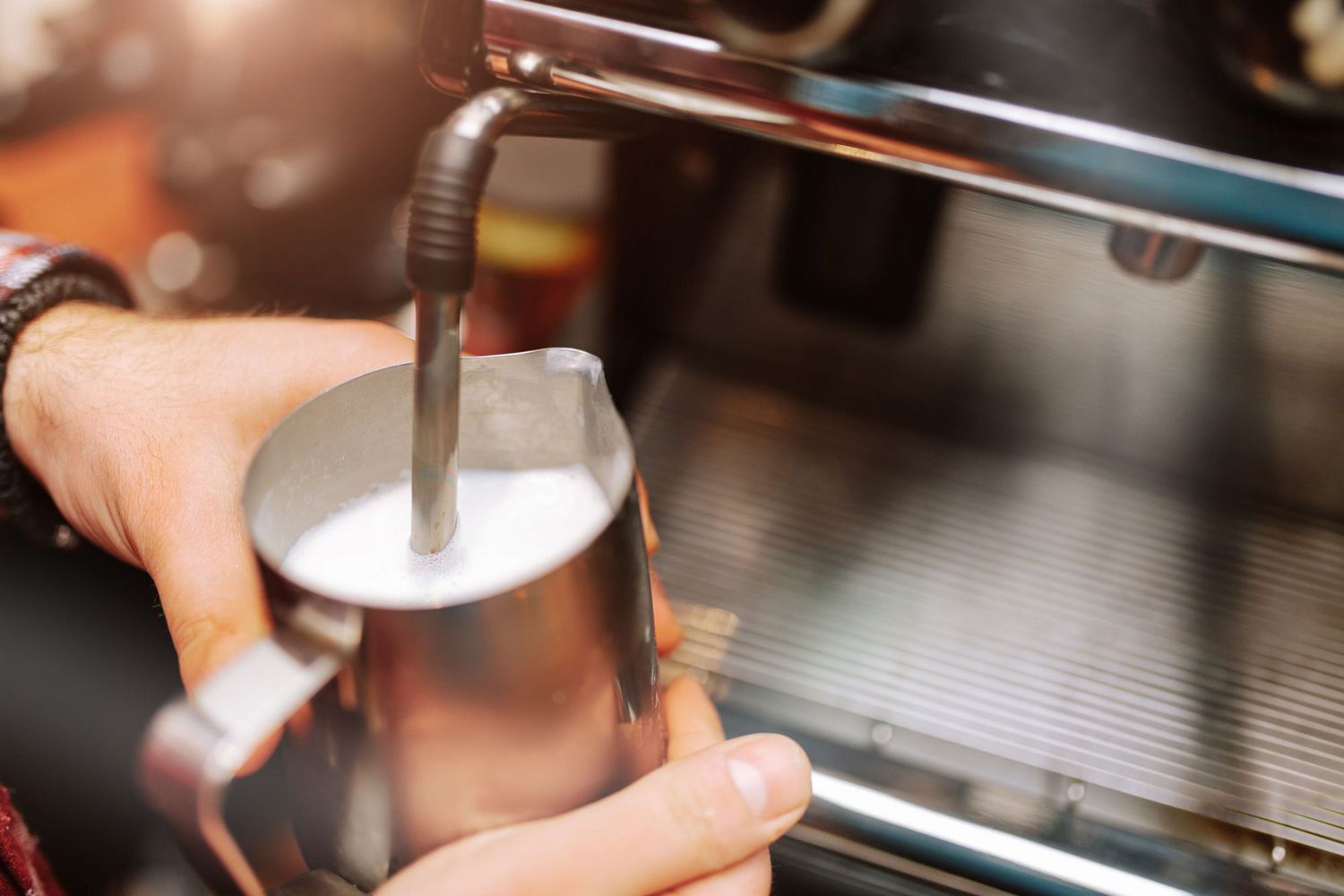 person using wand on espresso machine to froth milk or cream