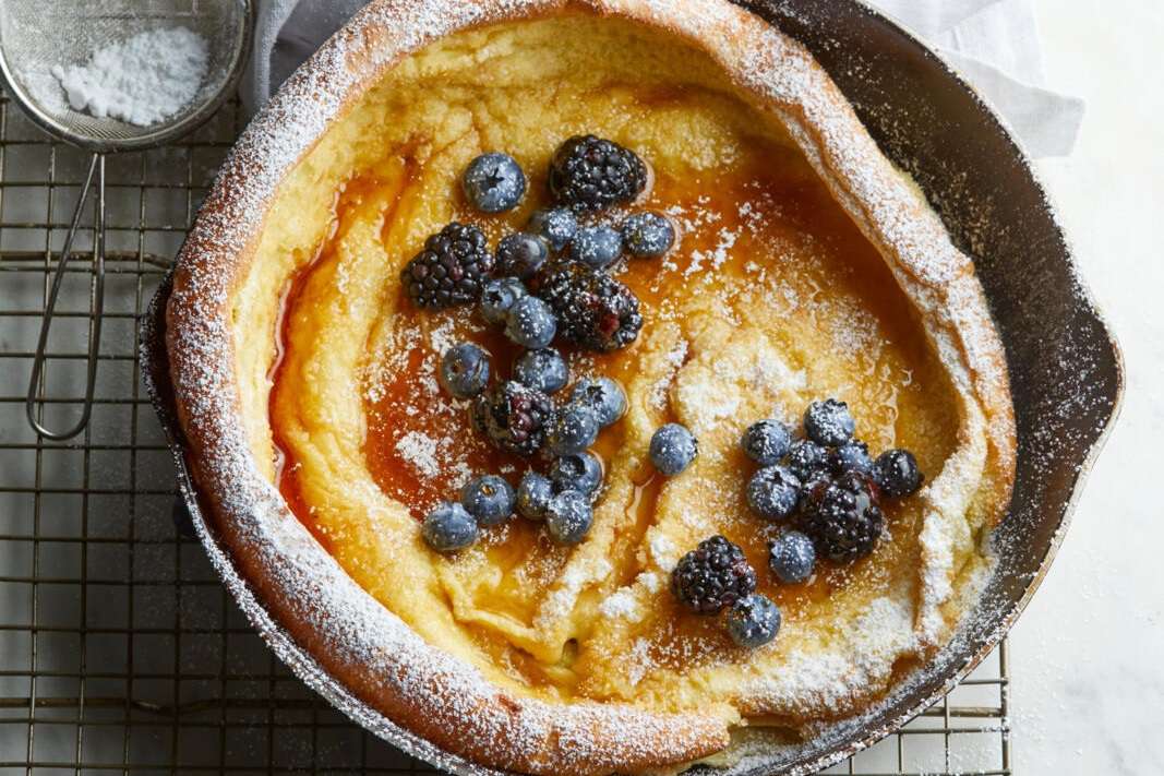 overhead view of a dutch baby pancake baked in a skillet and topped with powdered sugar, berries, and syrup