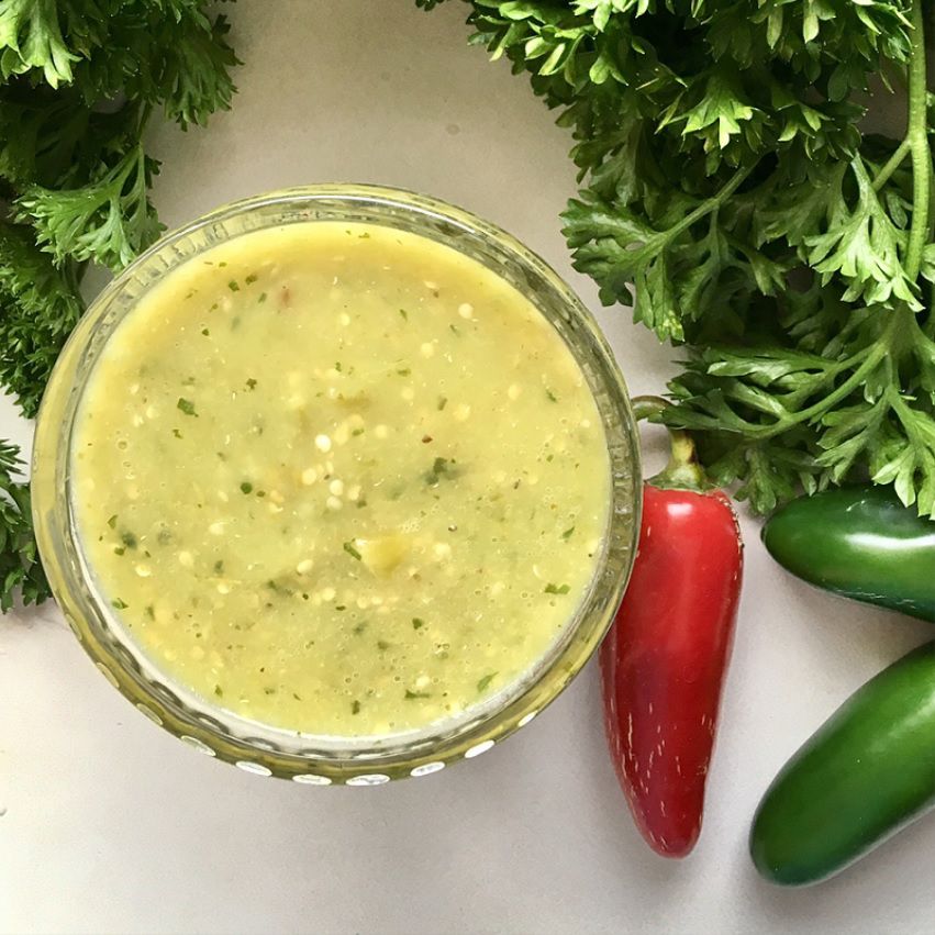 salsa verde in a glass bowl with red and green chile peppers on the side