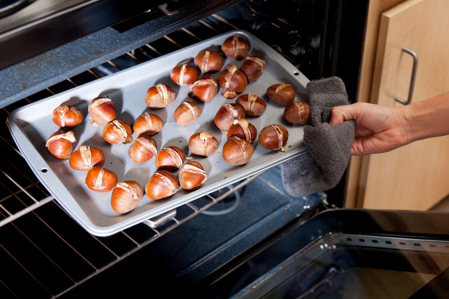 person taking baking sheet out of oven with roasted chestnuts