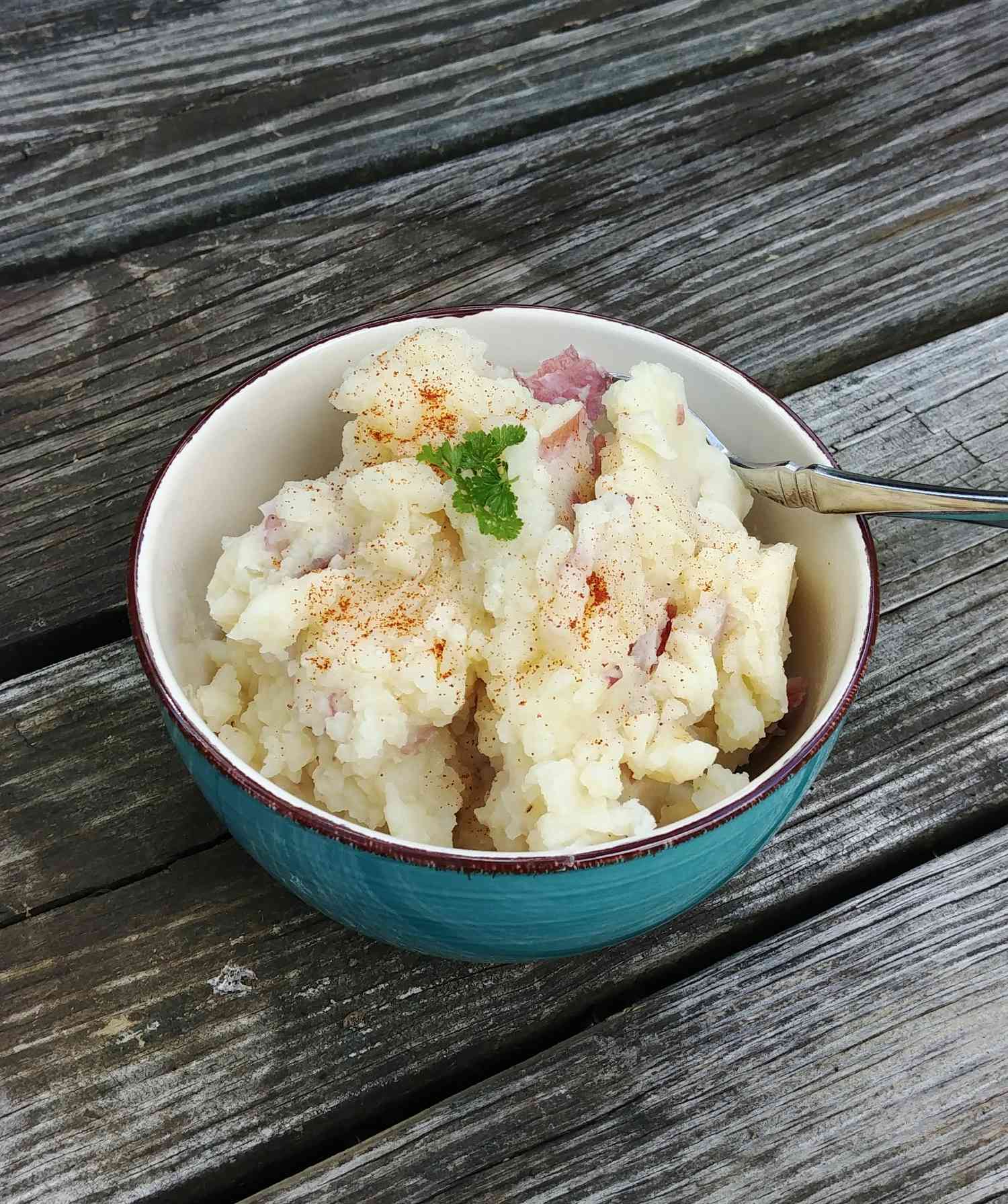 mashed potatoes with parsley and seasoning in ceramic bowl on wooden table