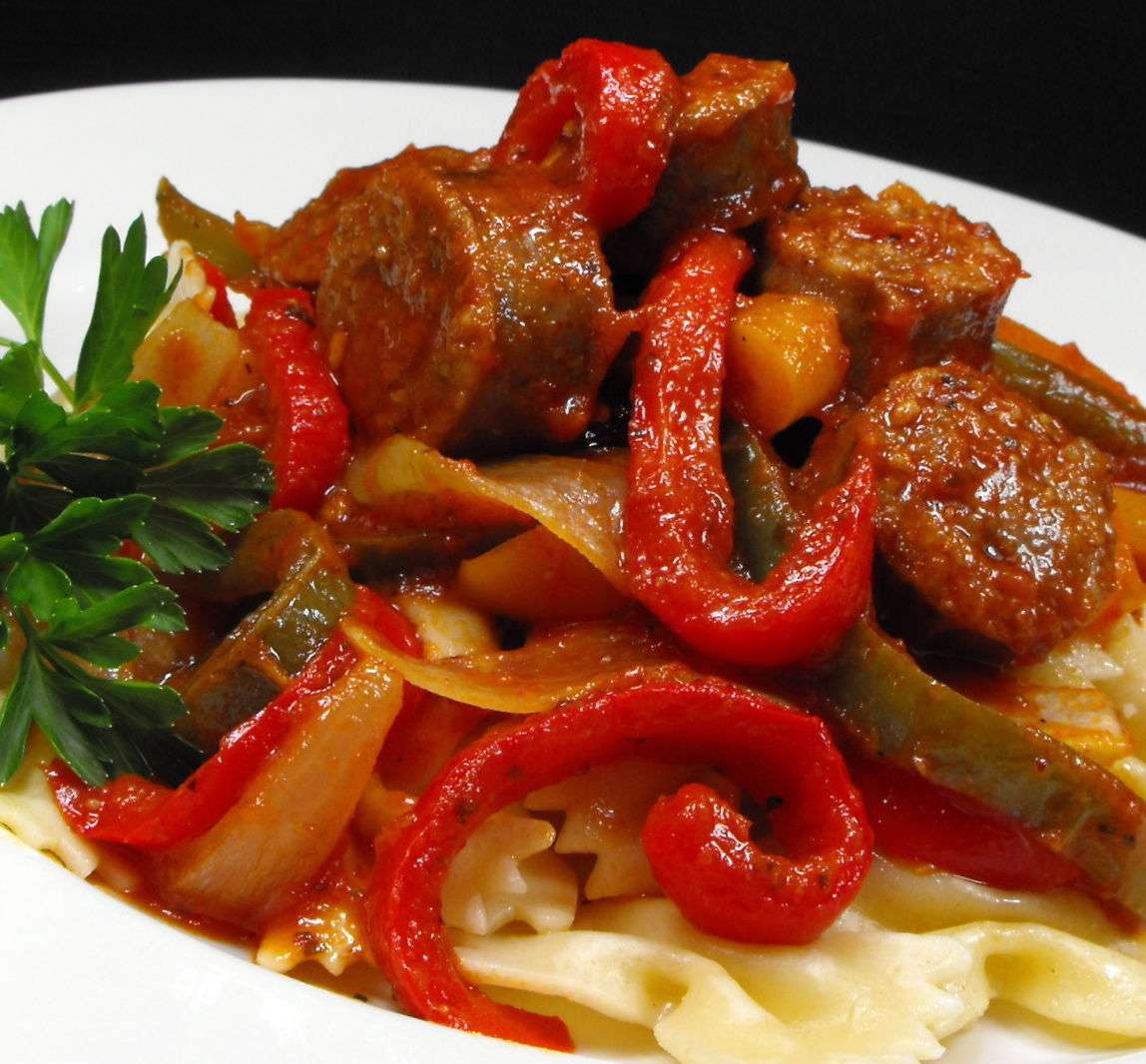 a colorful bowl of sliced sausage, red bell pepper, and onion over pasta, garnished with Italian parsley