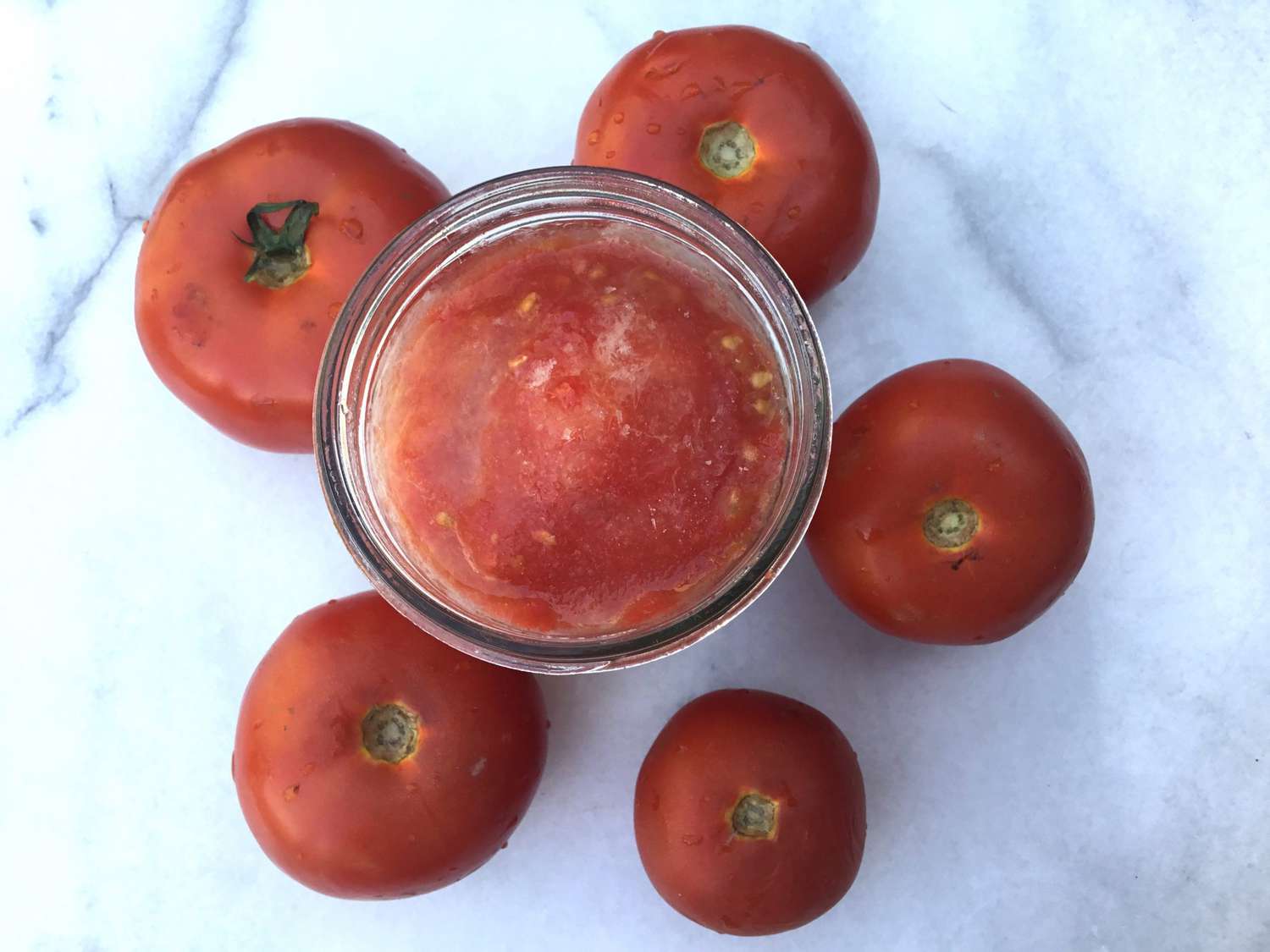 frozen tomatoes in jar with whole tomatoes around it