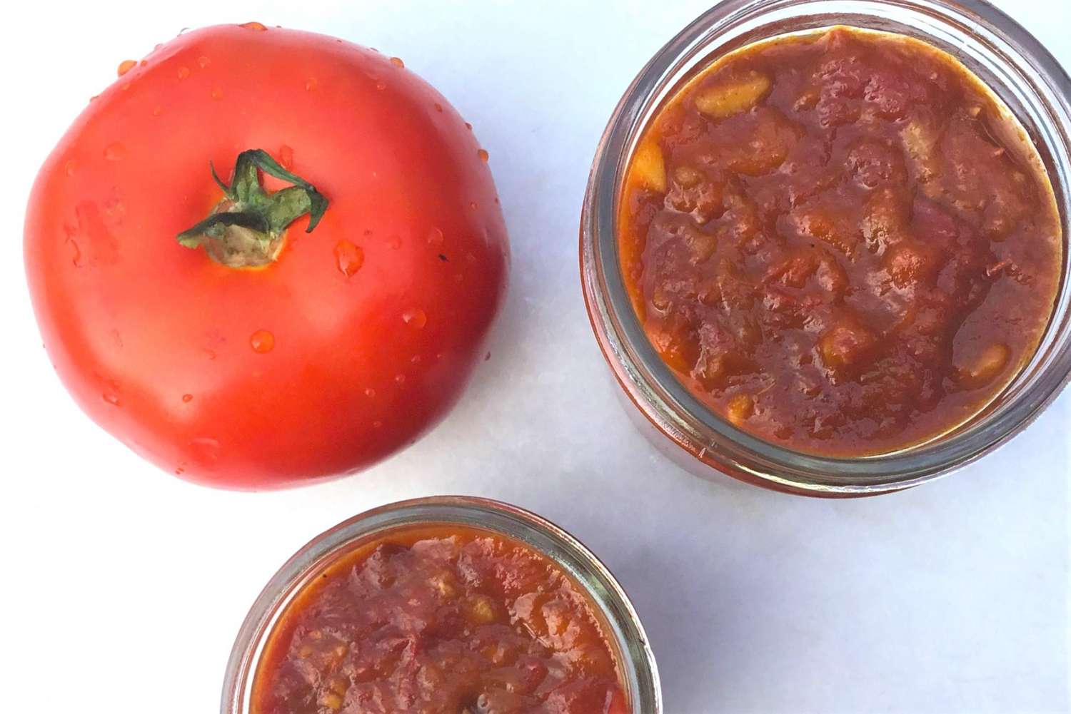 two jars of tomato jam with a tomato to the side
