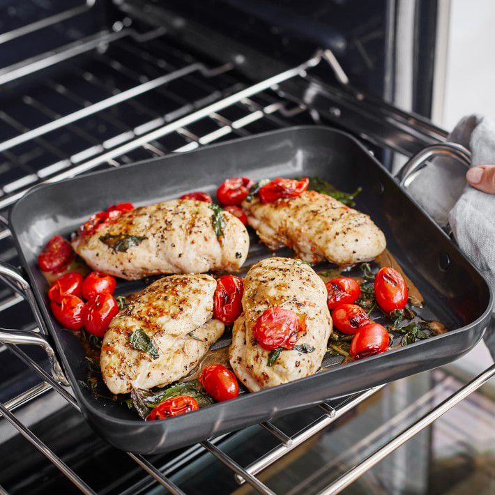 square grill pan with two handles with chicken breasts and tomatoes inside going into the oven