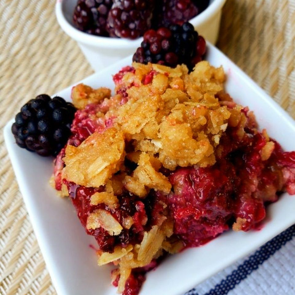 close up of homemade Blackberry Crisp on a square plate with fresh blackberries in a bowl