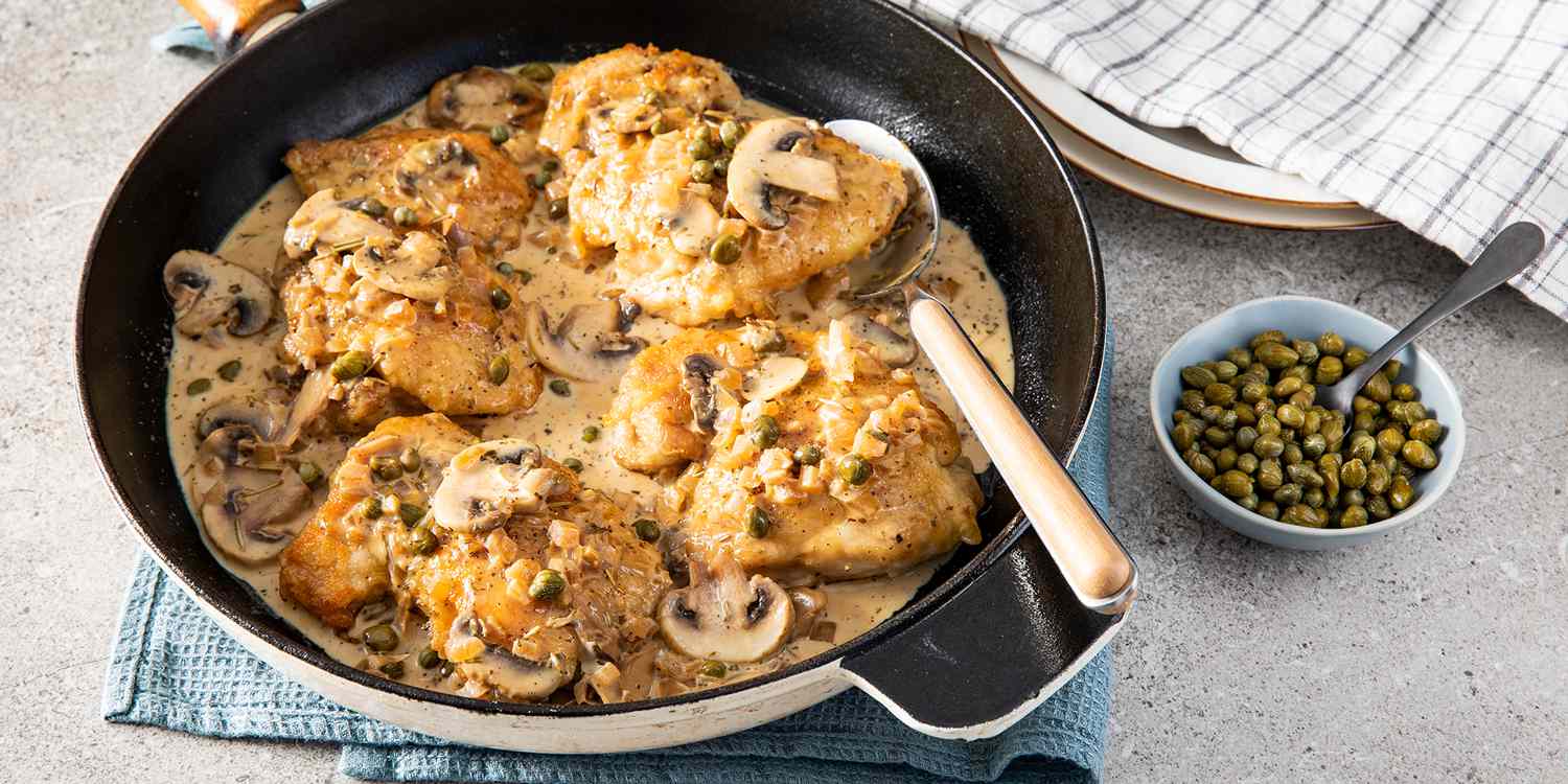 Looking into a skillet of perfect chicken, covered in a mushroom cream sauce, capers, and onions.