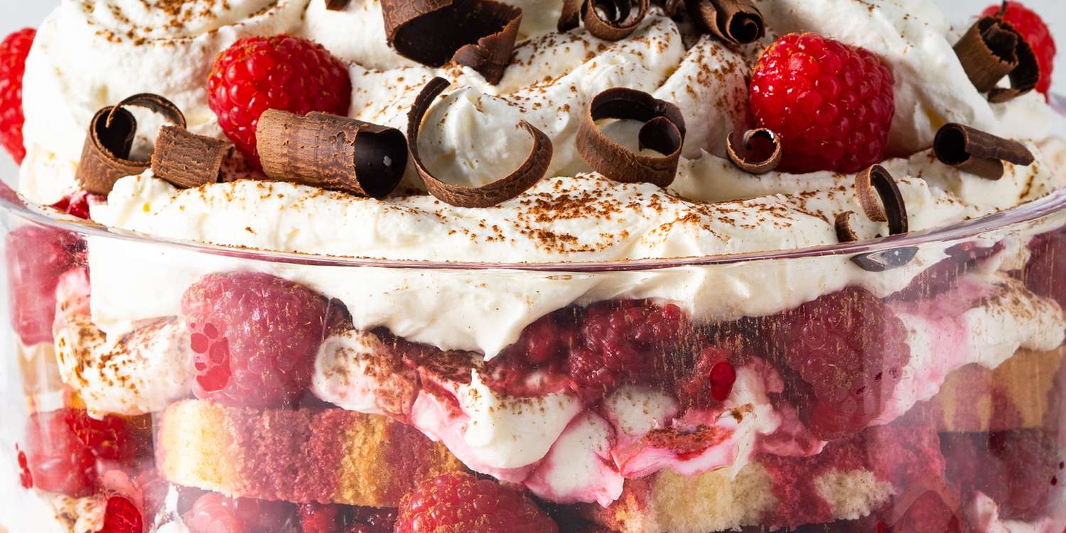 Looking into all the beautiful layers of a raspberry triffle topped with fresh whipped cream, fresh raspberries and chocolate curls.