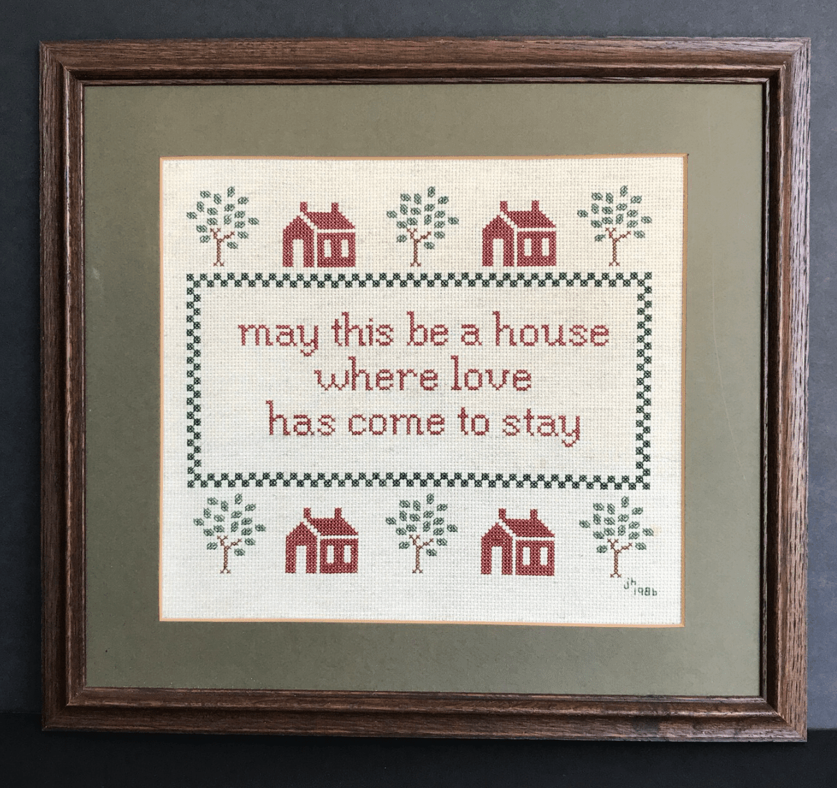 cross stitch that says "may this be a house where love has come to stay" with houses and trees around it