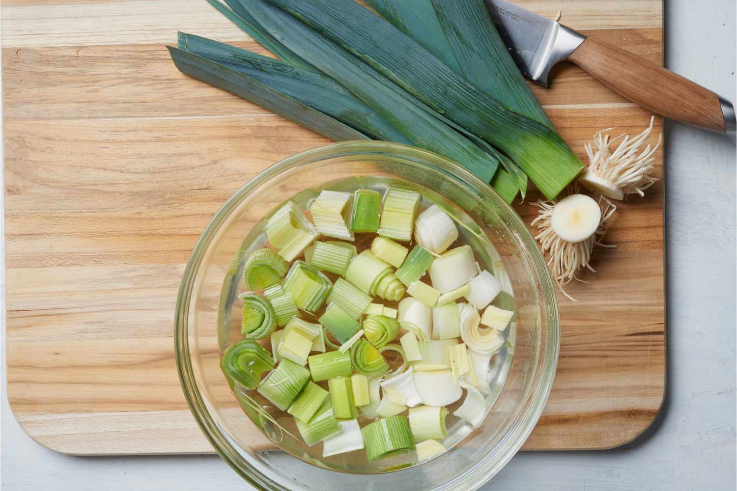 leeks on cutting board with sliced leeks in water bowl
