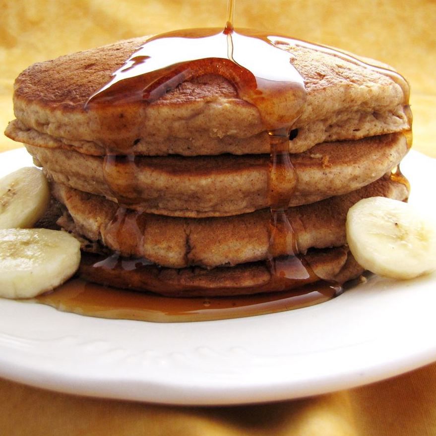 stack of whole wheat pancakes with syrup and banana slices