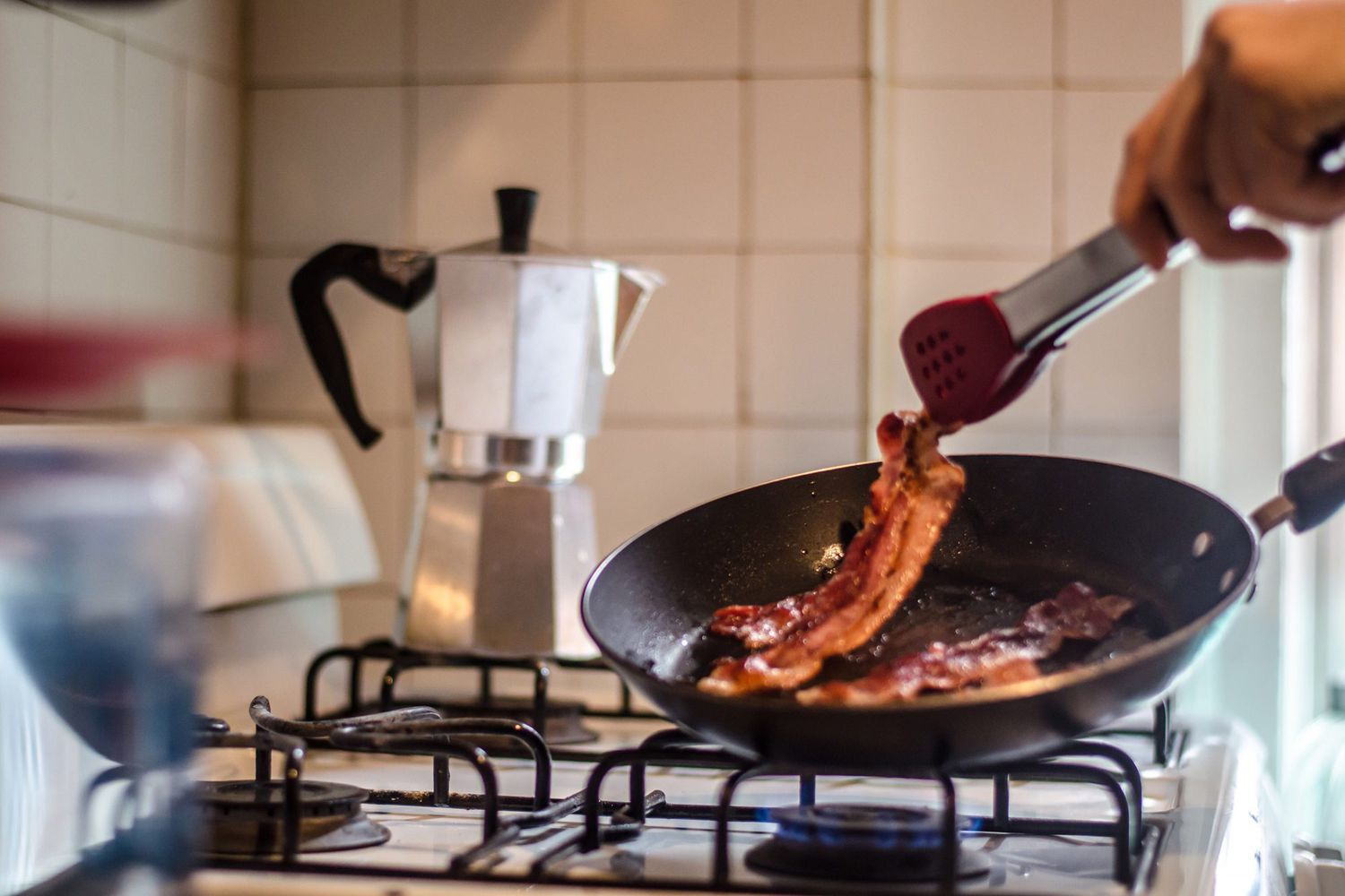 person flipping bacon in a frying pan over gas stove