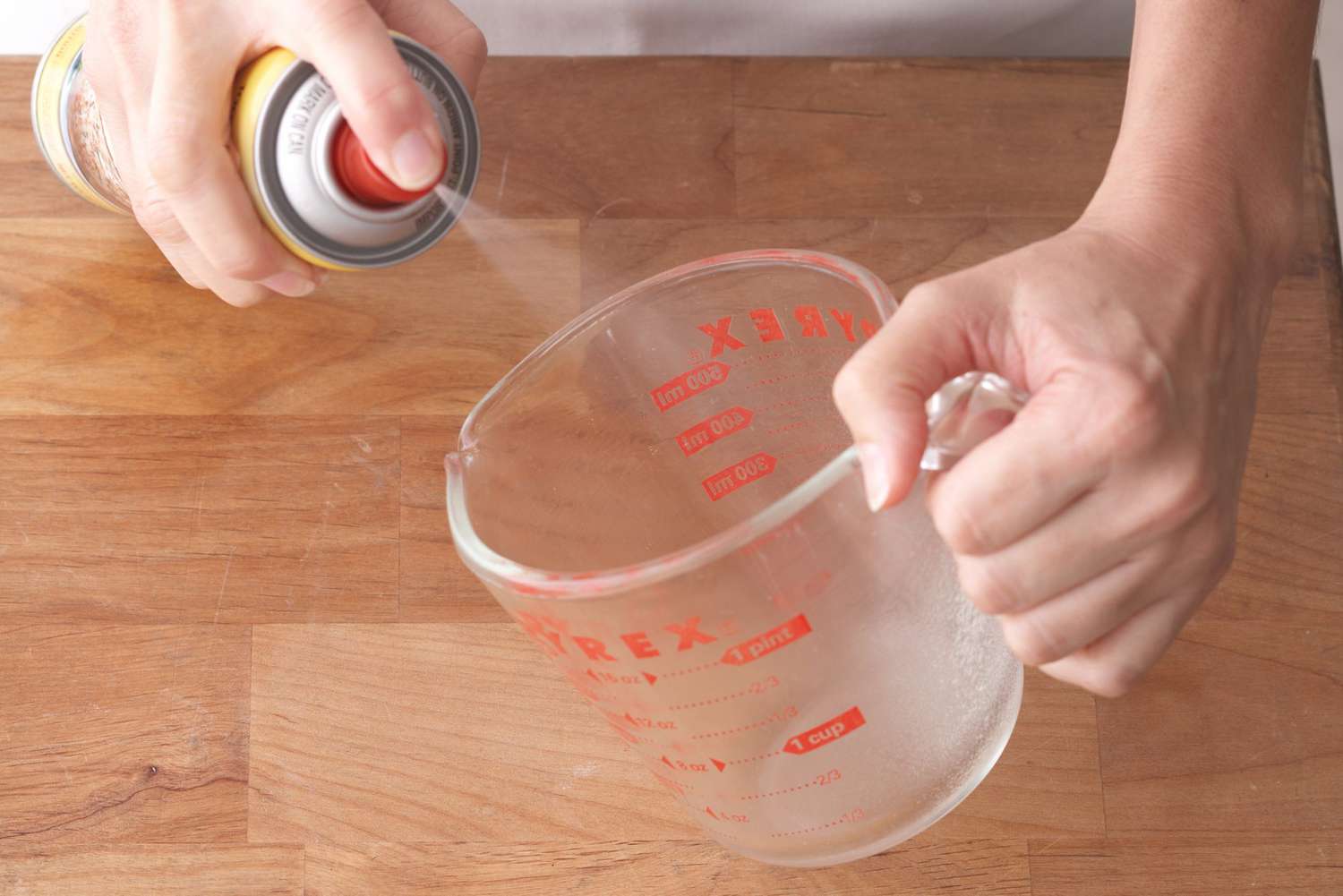 person spraying pyrex liquid measuring cup with pam