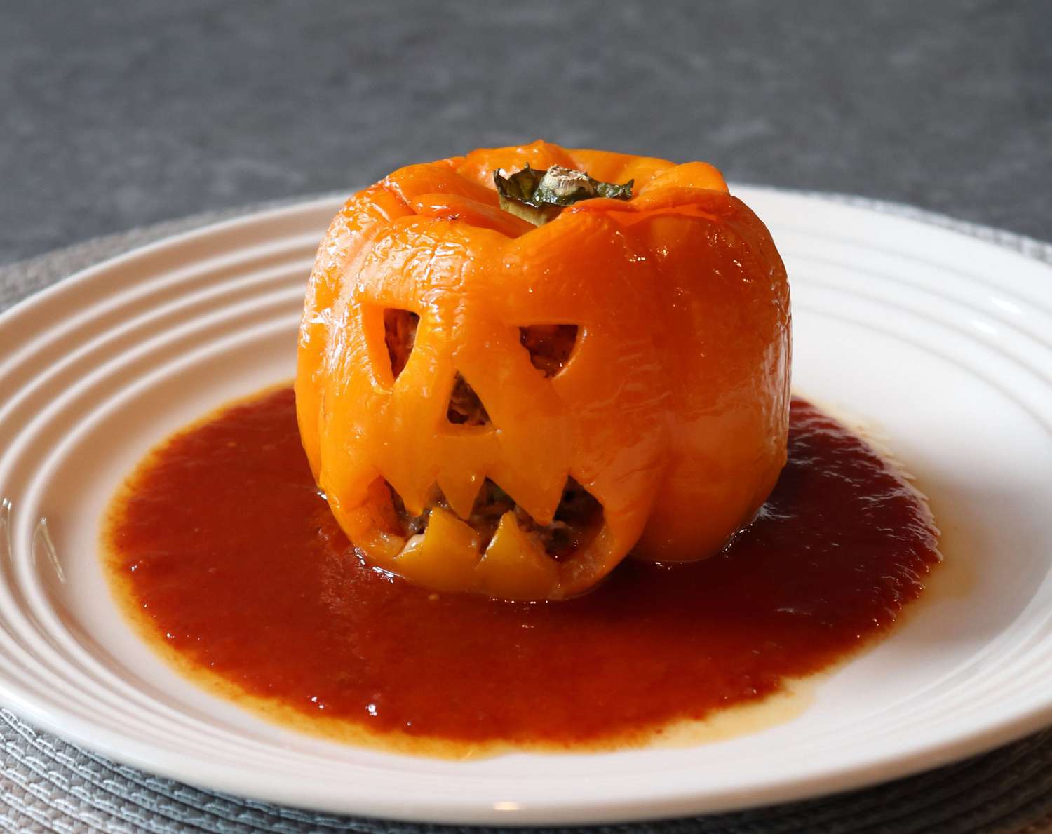 an orange bell pepper cut to look like a jack o' lantern face in a pool of tomato sauce on a white plate