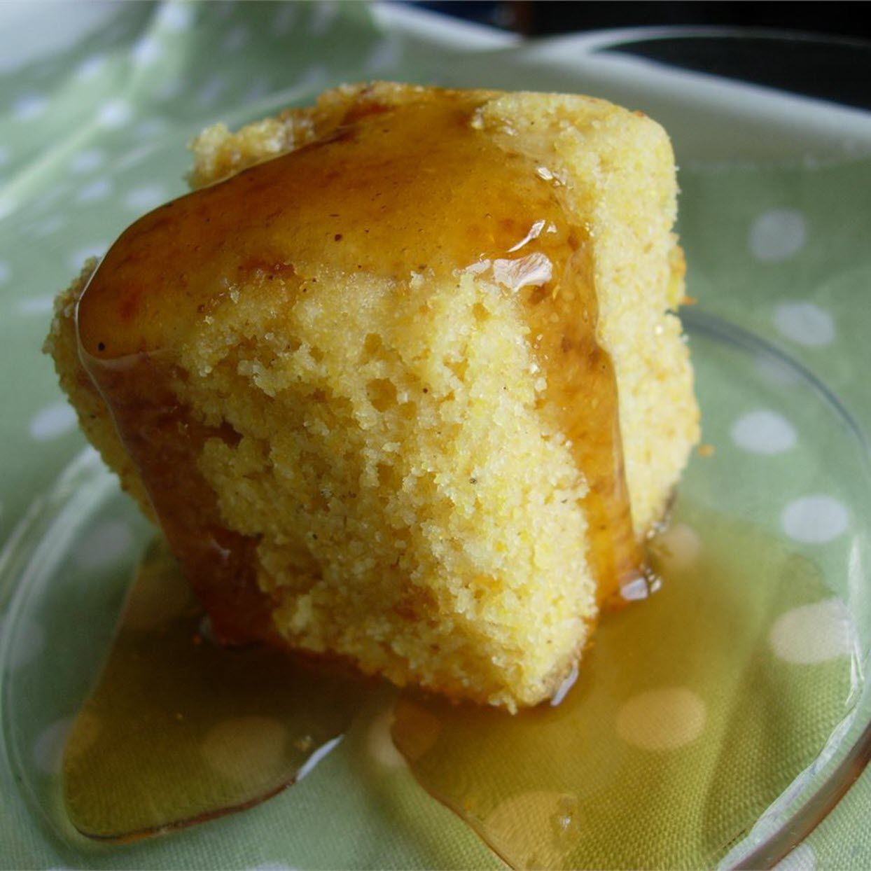 a thick square of cornbread with honey dripping down its sides on a green plate