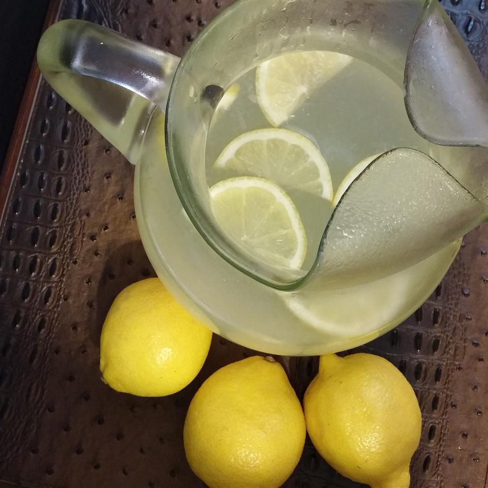 top-down view of a glass pitcher of lemonade garnished with lemon slices, with whole lemons on the side
