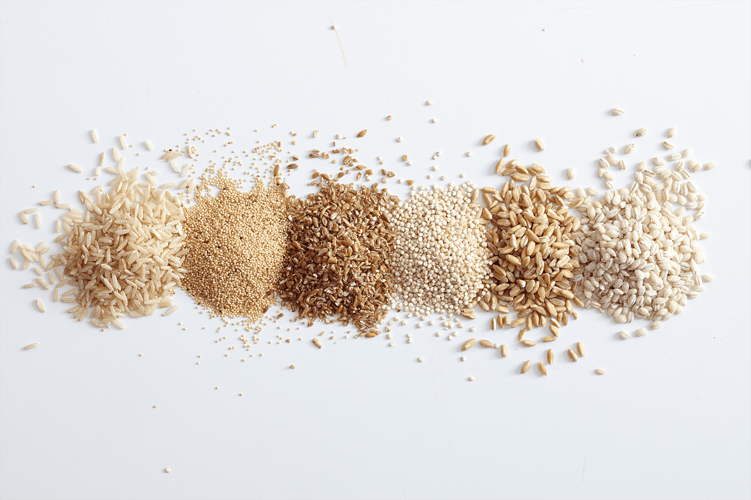 six piles of whole grains and rices side by side on a white background
