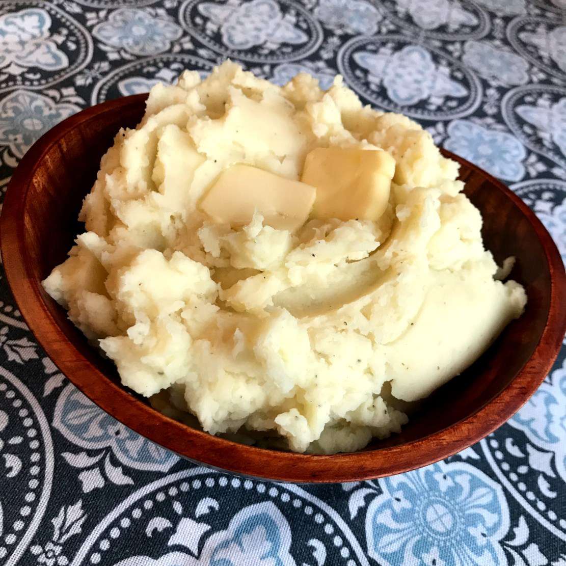 a wooden bowl of mashed potatoes with two pats of butter