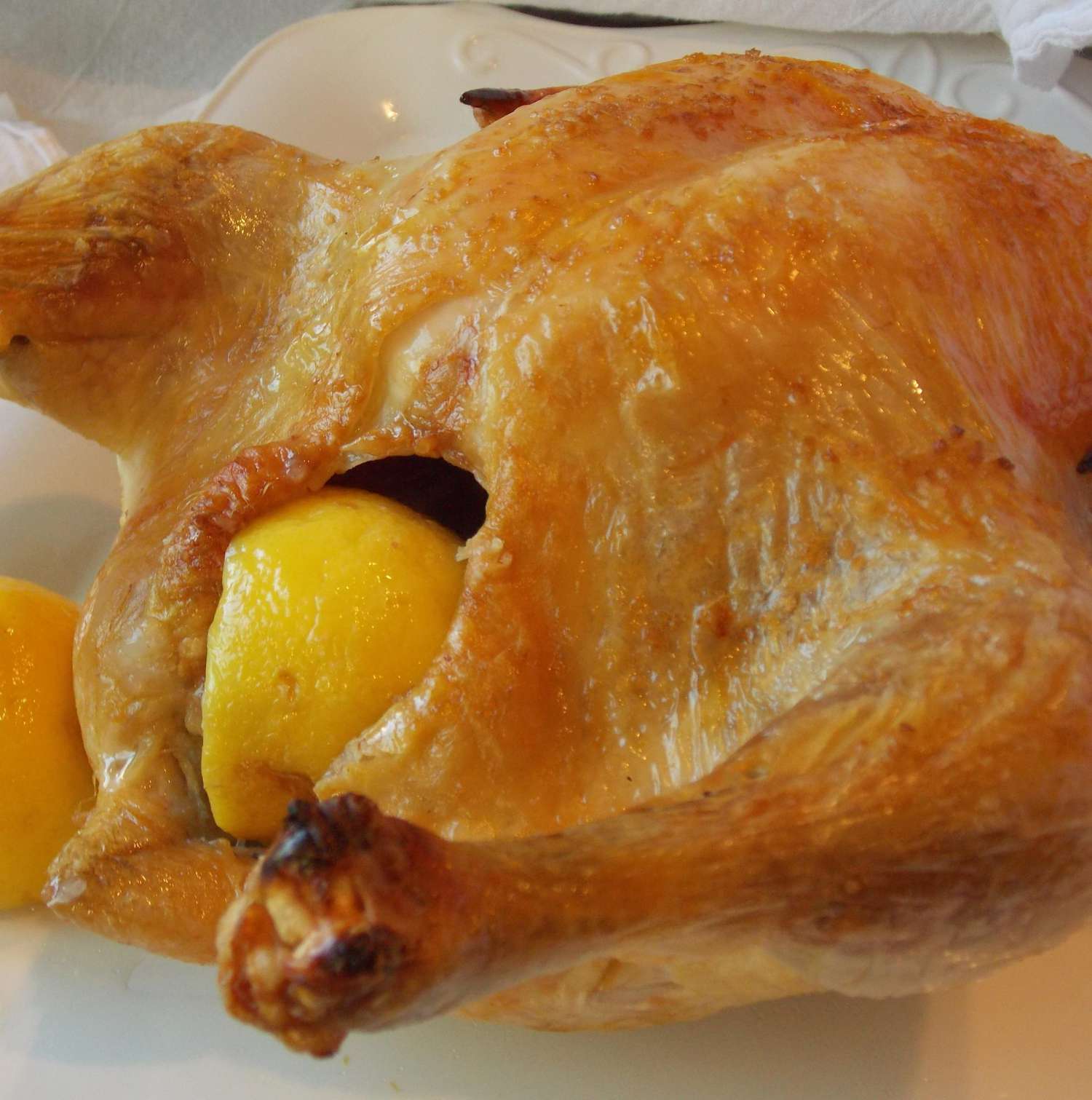 closeup of a golden brown roast chicken with a halved lemon in the cavity