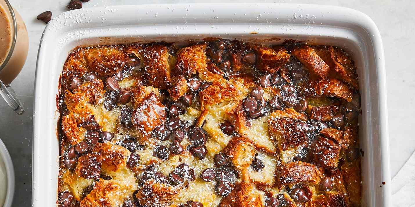 Overhead view on chocolate croissant bread pudding in a white casserole dish.The bread pudding is perfectly golden brown and studded with chocolate chips.