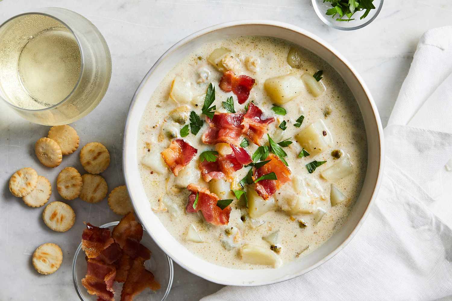 overhead view of New England Clam Chowder II recipe in a bowl garnished with bacon bits, parsley, and oyster crackers