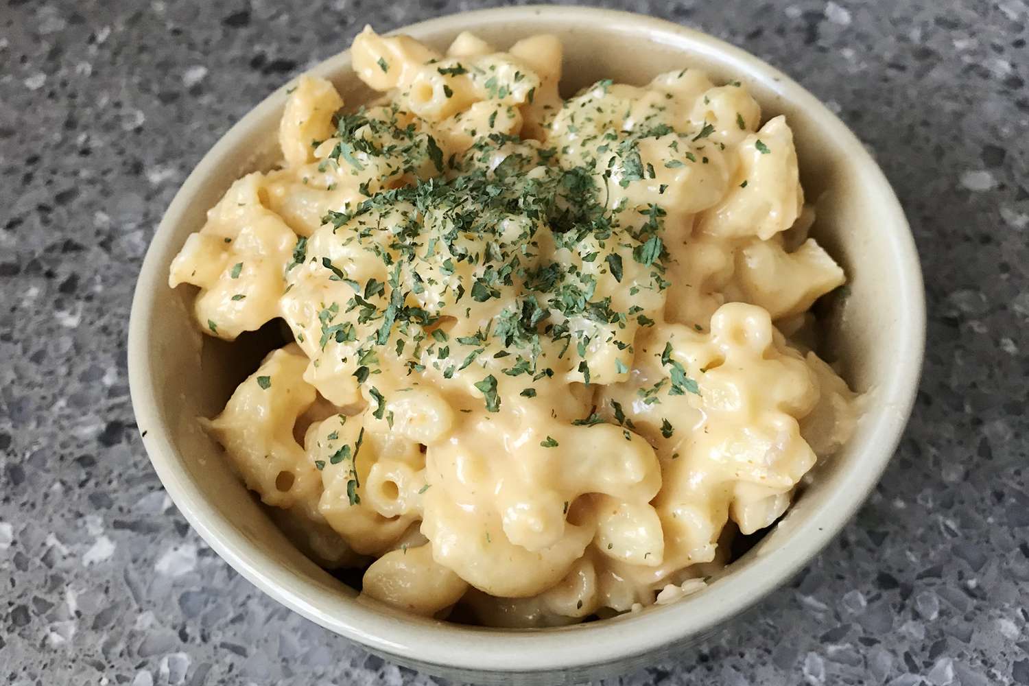 a close up view on a bowl of simple creamy macaroni and cheese topped with fresh parsley.