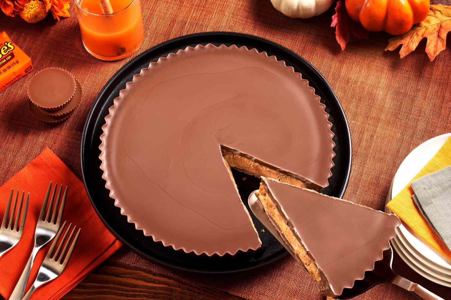 a reese's pie with a wedge cut sits on a table with candles and pumpkins