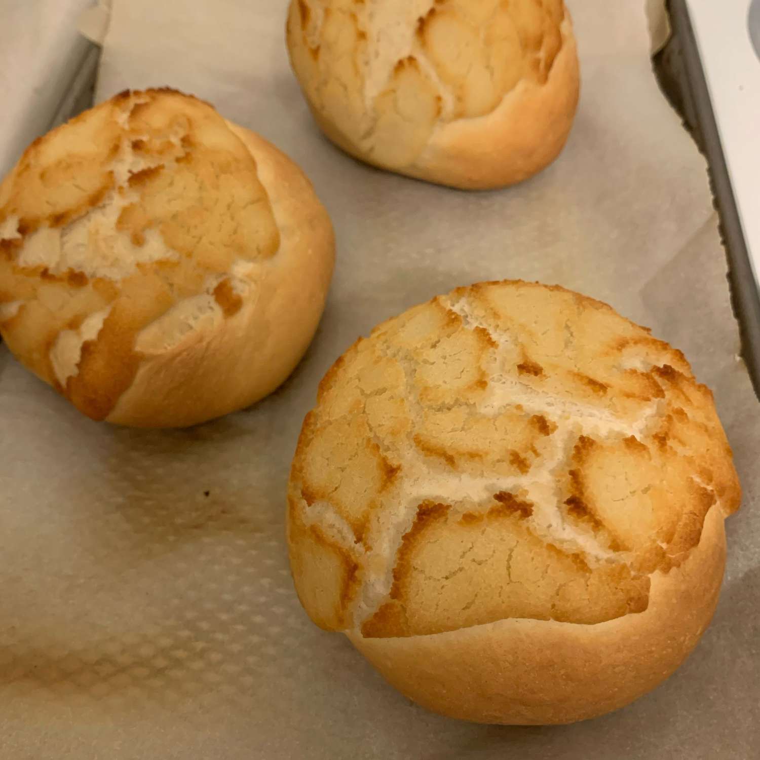 top-down view of dinner rolls with a crackle top on a parchment-lined baking sheet