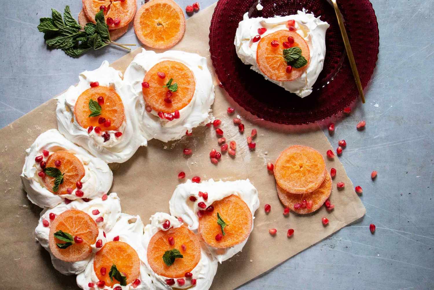 Pavlova wreath topped with lemon curd, candied citrus, pomegranate seeds, and mint leaves