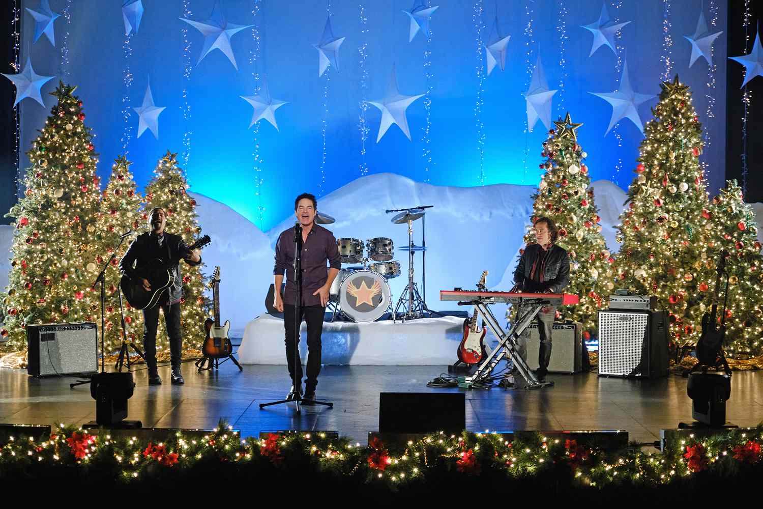 a three-man band performing on a stage decorated with Christmas trees