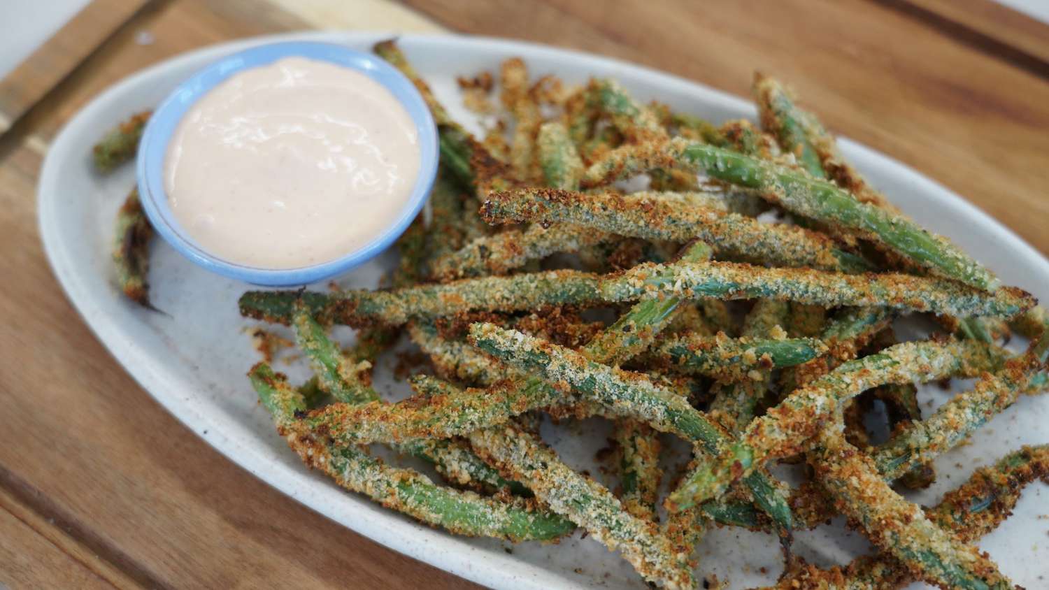 parmesan crusted green beans on a white plate with a small bowl of dipping sauce