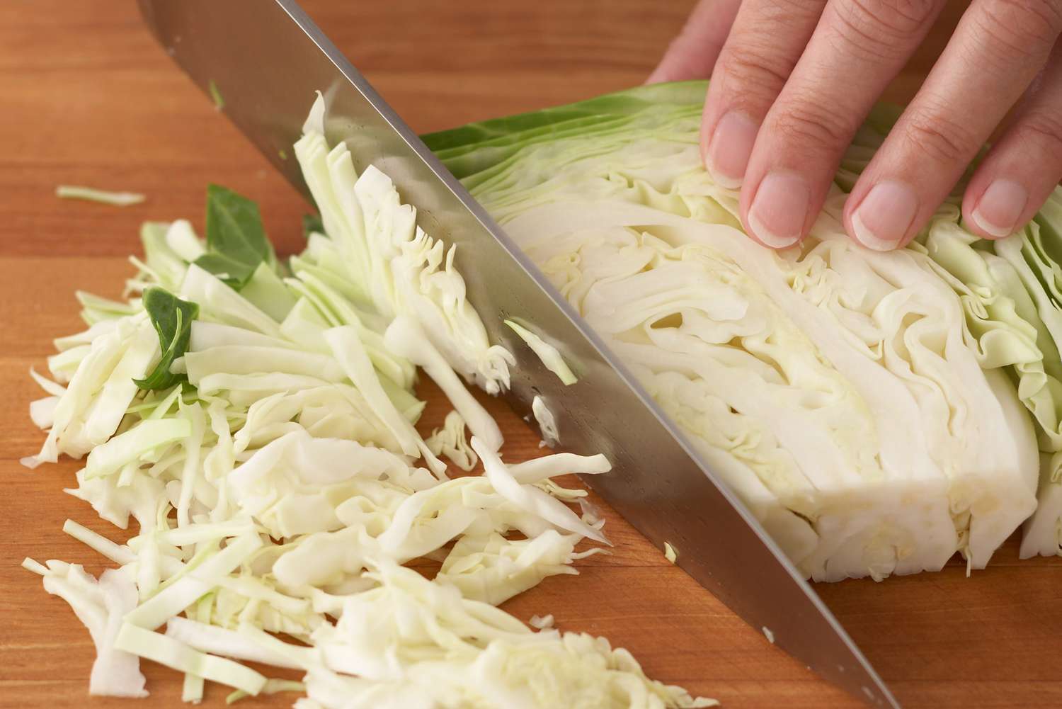 person holding knife slicing cabbage wedge into thin shreds