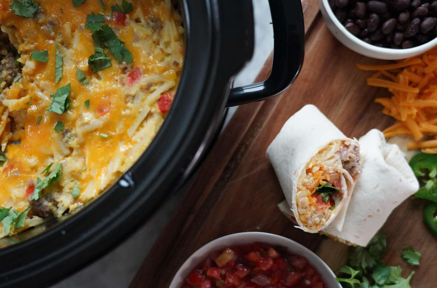 breakfast burrito next to a slow cooker full of egg, potato, and cheese mixture