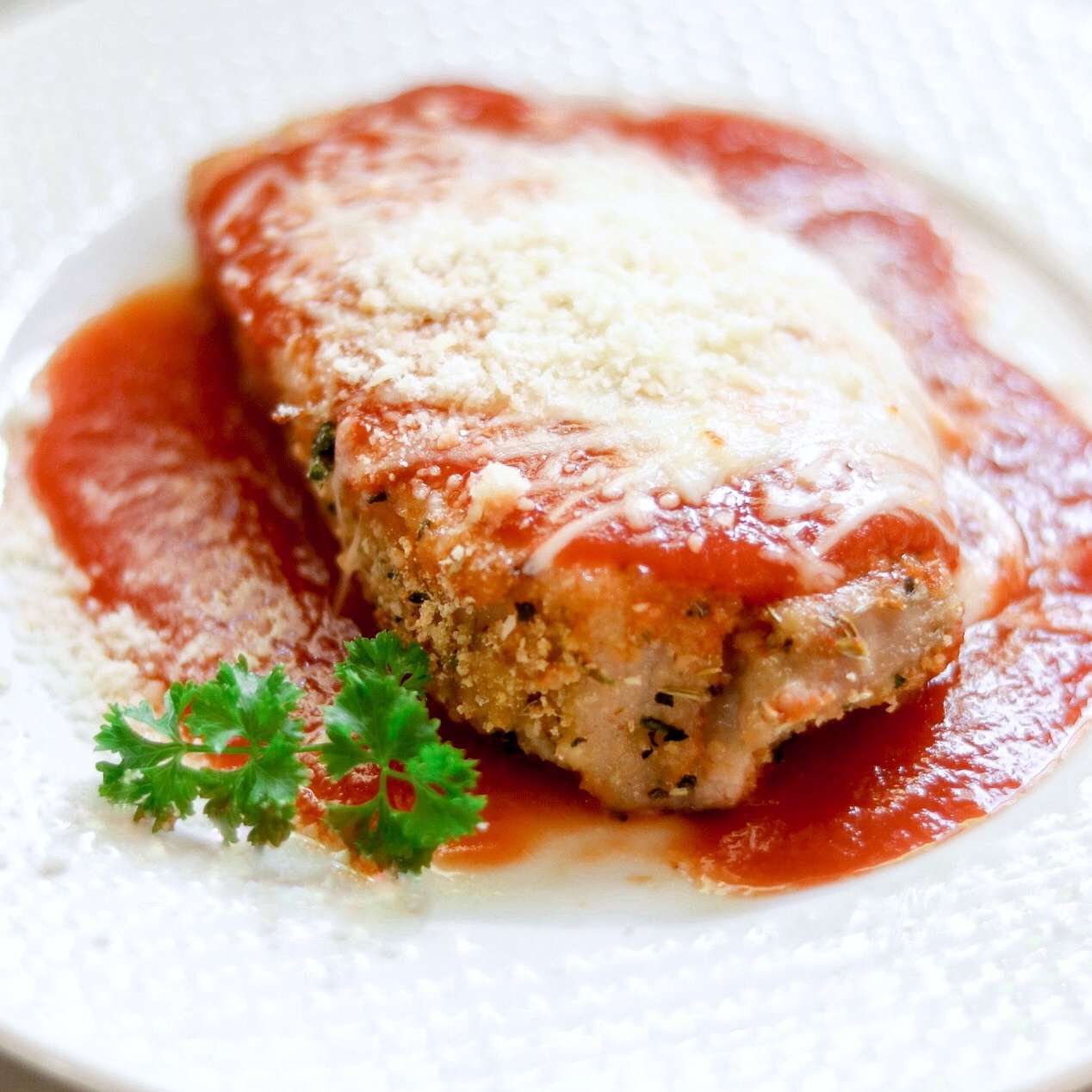 chicken parmesan with parsley garnish on a white plate