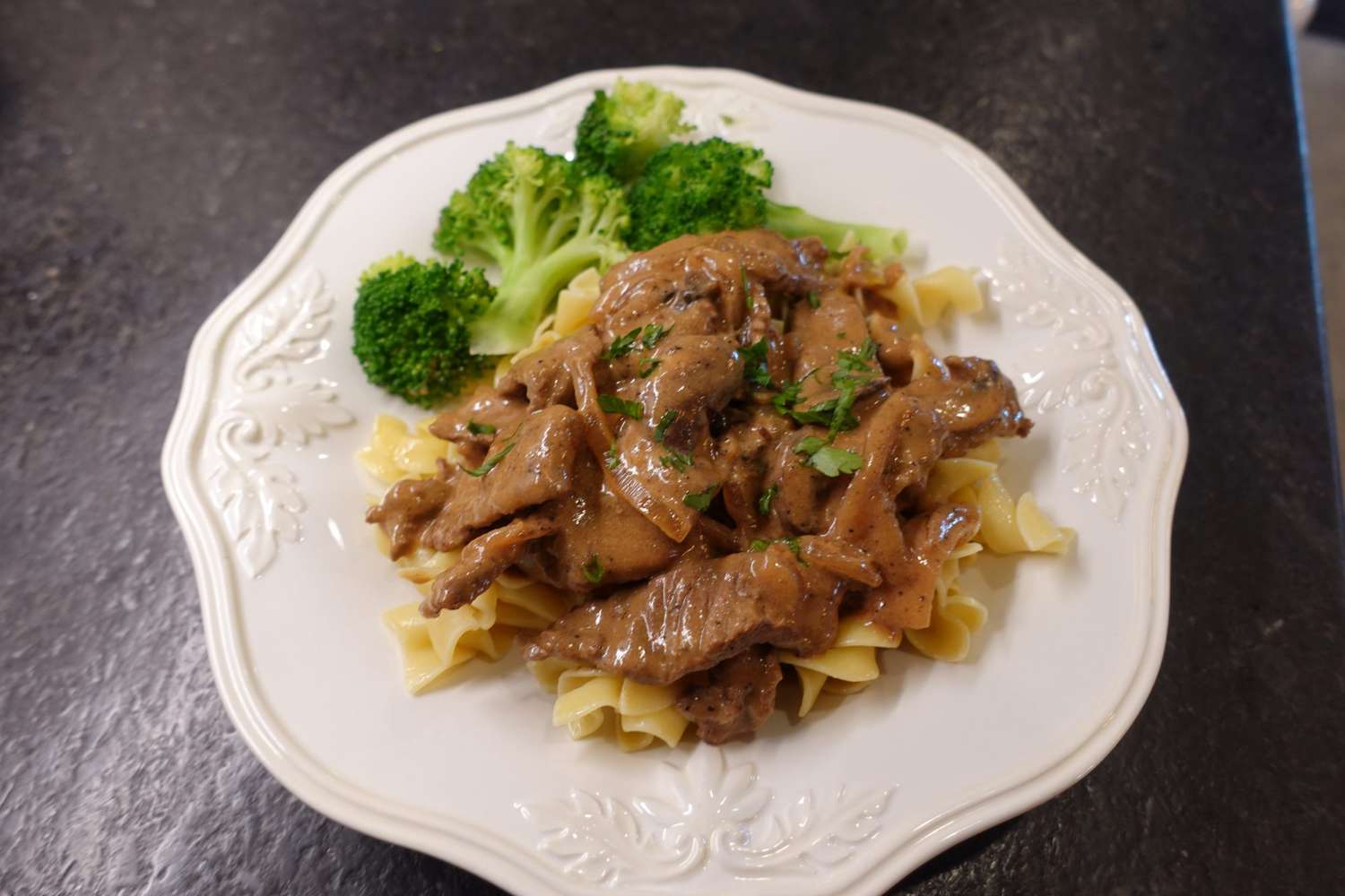 beef stroganoff over egg noodles with a side of broccoli on a white plate
