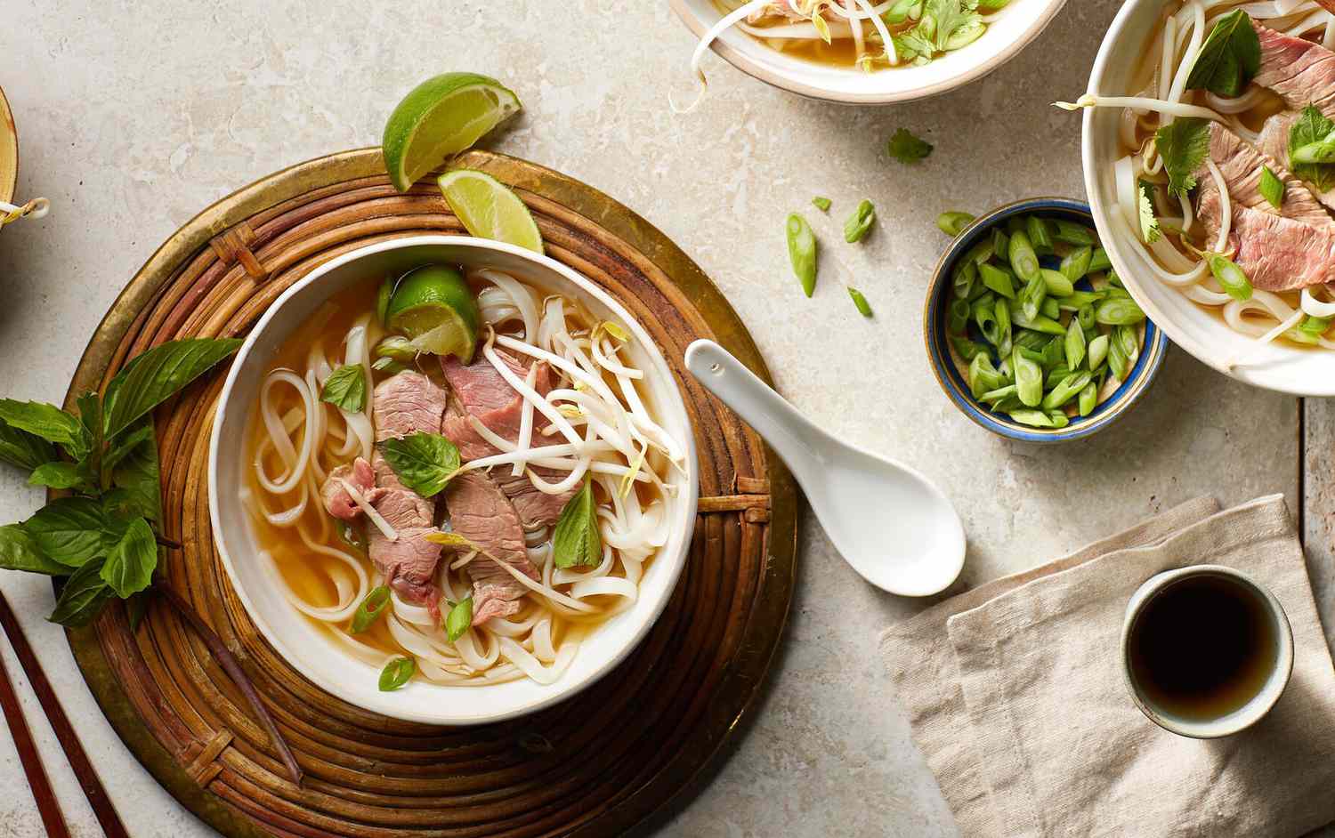 Rice noodles and thinly sliced beef in a bowl of beef broth, garnished with lime and basil