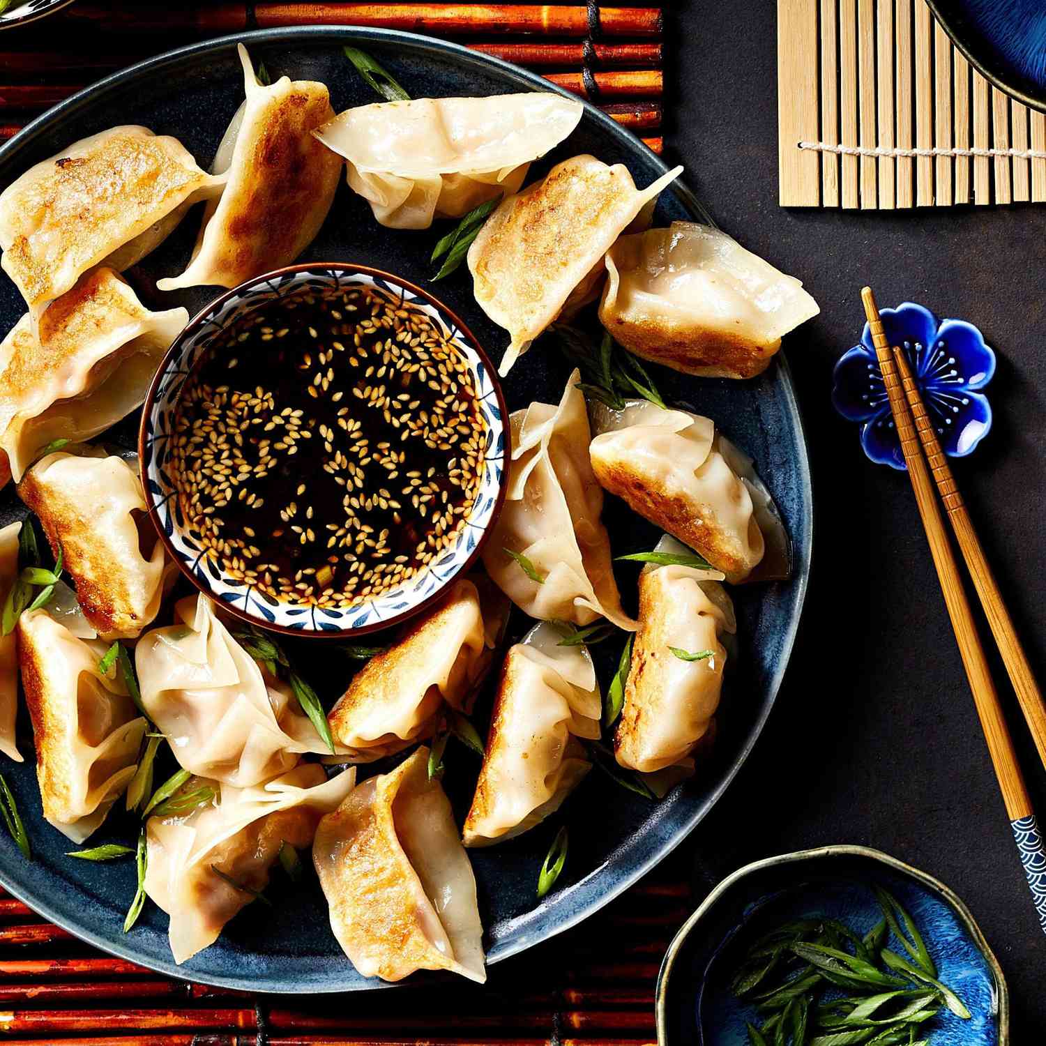 Dumplings on a blue platters surrounding a small bowl of dipping sauce