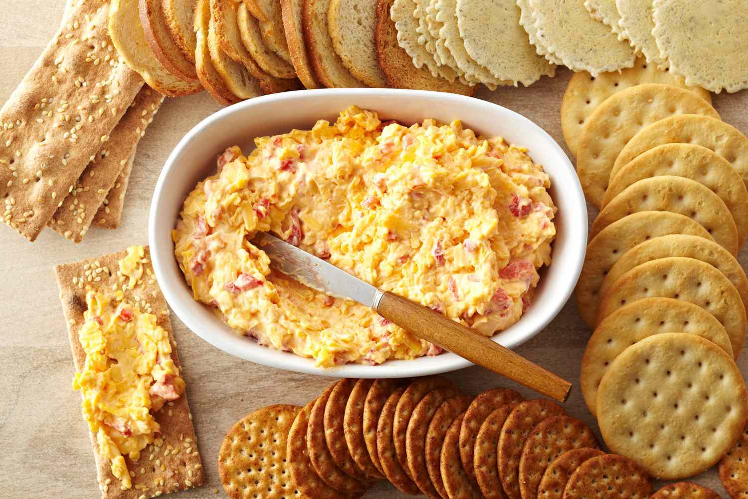 white dish with pimento cheese and spreading knife surrounded by variety of crackers