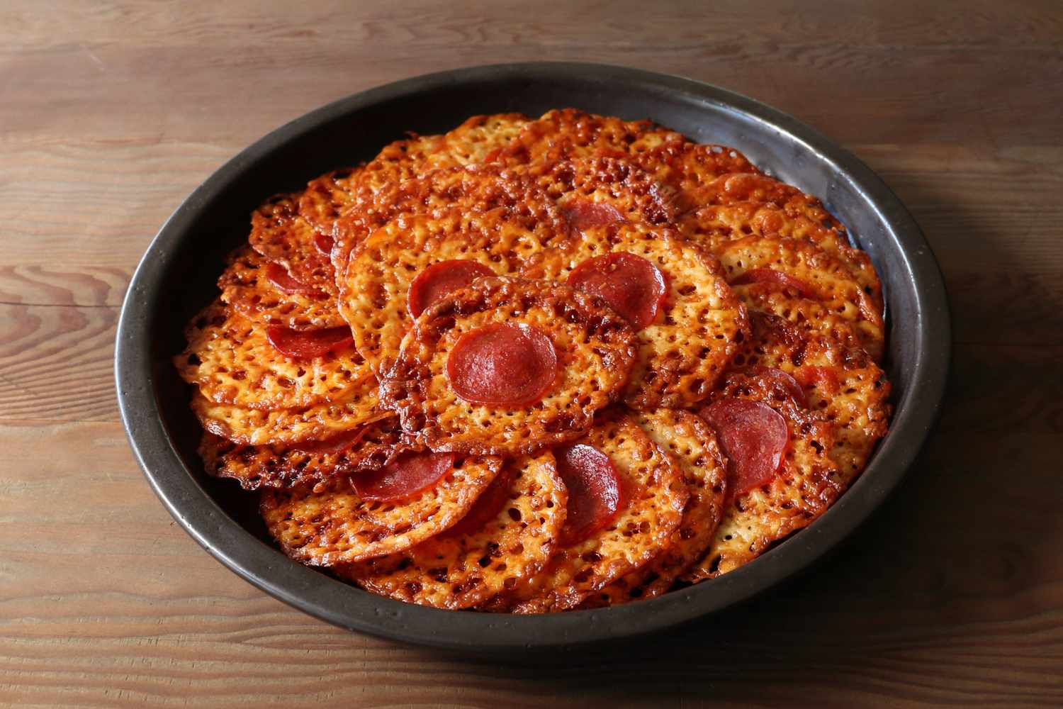 Pepperoni-topped melted cheese crisps stacked in a round black bowl